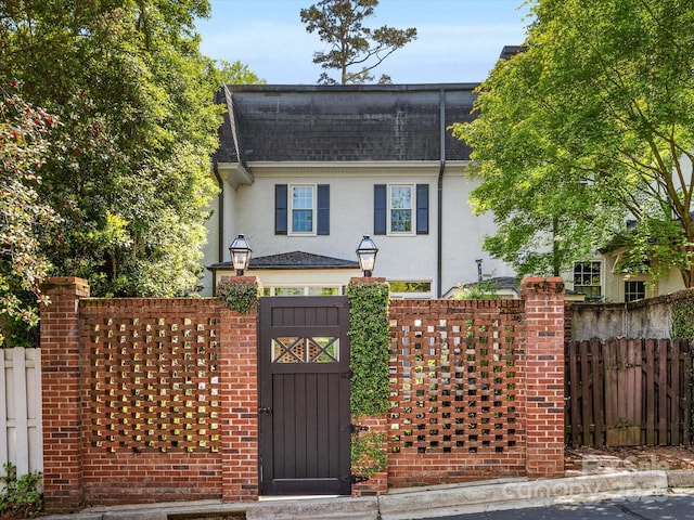 view of front of property featuring stucco siding, fence, a gate, and roof with shingles