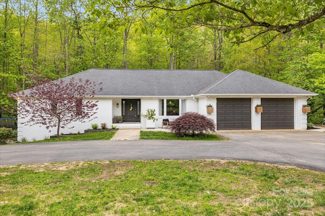 ranch-style home with asphalt driveway, a garage, a shingled roof, and a front yard