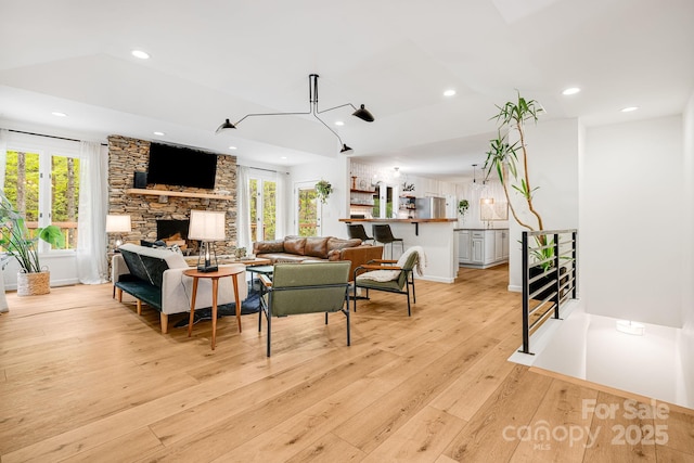 living room featuring recessed lighting, light wood finished floors, a stone fireplace, and lofted ceiling