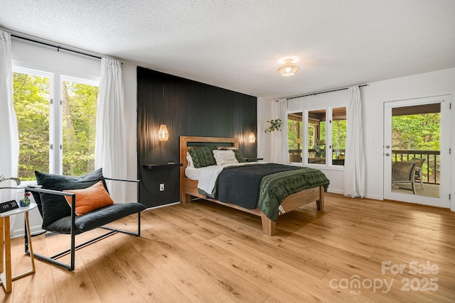 bedroom with access to outside, light wood-style flooring, a textured ceiling, multiple windows, and wood walls
