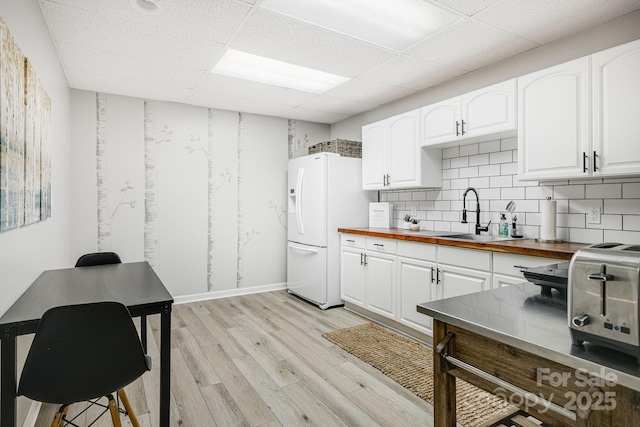 kitchen featuring white fridge with ice dispenser, butcher block counters, light wood-style floors, a sink, and a drop ceiling