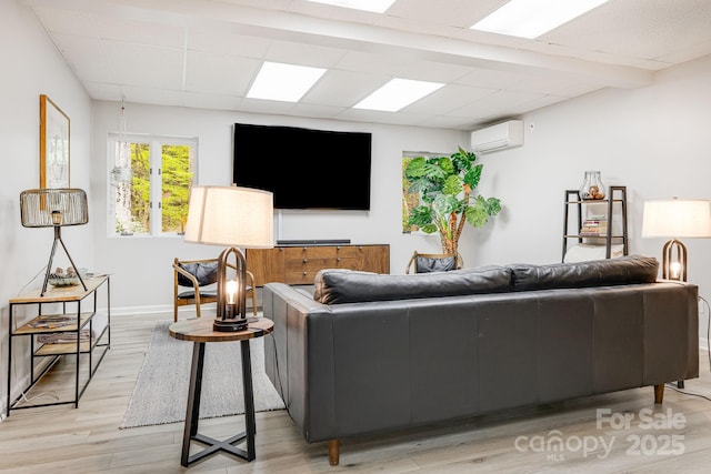 living room featuring an AC wall unit, a paneled ceiling, light wood-style floors, and baseboards