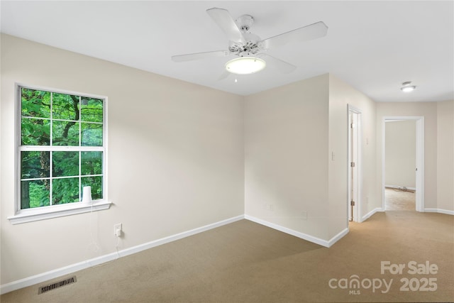 carpeted spare room featuring baseboards and a ceiling fan