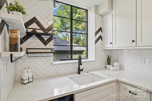 kitchen with a sink, backsplash, white cabinetry, and light countertops