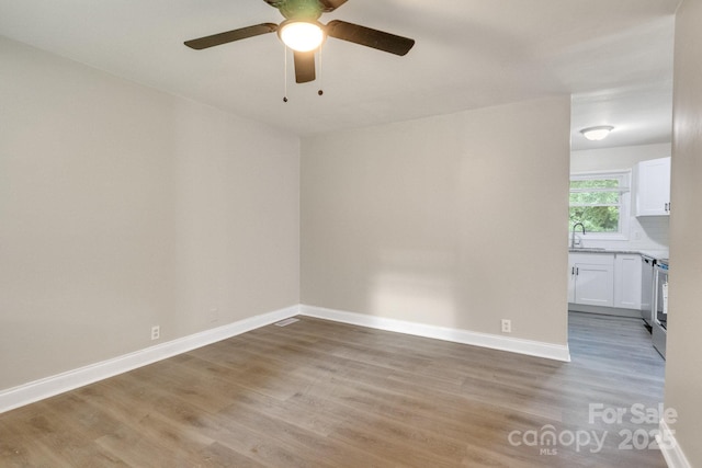 unfurnished room featuring a sink, light wood-style floors, ceiling fan, and baseboards