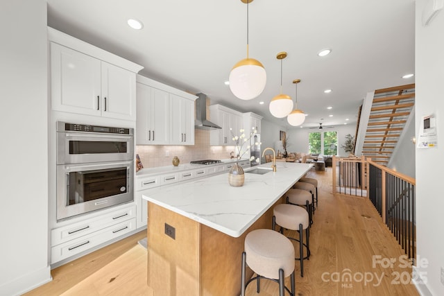 158 Mattoon St, Charlotte, NC 28216 - kitchen with appliances with stainless steel finishes, a sink, wall chimney range hood, light wood finished floors, and a center island with sink