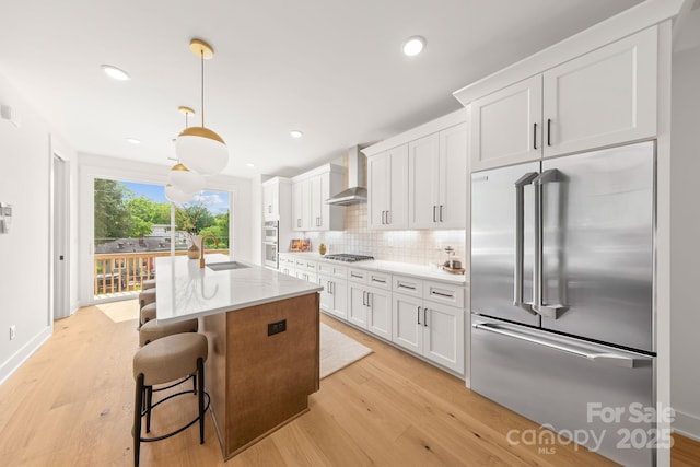 158 Mattoon St, Charlotte, NC 28216 - kitchen with stainless steel appliances, wall chimney range hood, light wood-style floors, decorative backsplash, and a kitchen island with sink