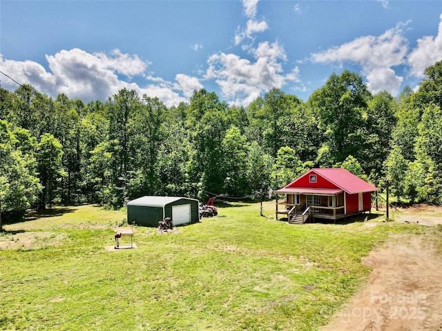 view of grassy yard with an outdoor structure, a forest view, and a garage