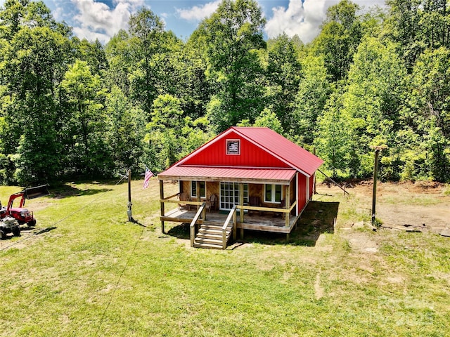 rustic home with metal roof, a front yard, covered porch, and a view of trees