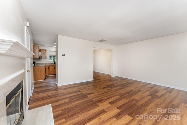 unfurnished living room featuring dark wood-type flooring, a fireplace, baseboards, and a sink
