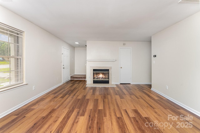 unfurnished living room featuring wood finished floors, a glass covered fireplace, and baseboards