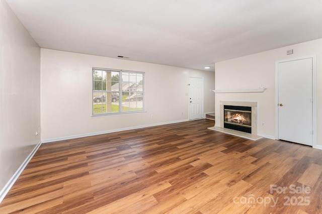 unfurnished living room featuring wood finished floors, a glass covered fireplace, and baseboards