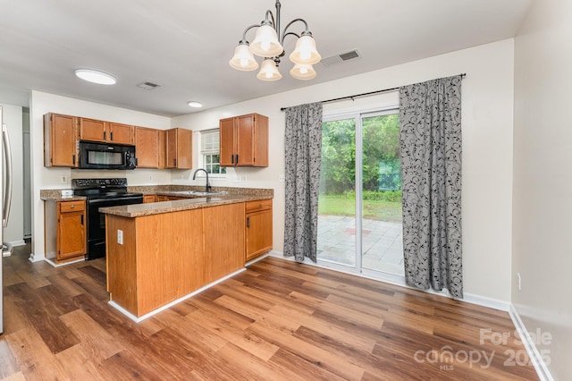 kitchen with black appliances, wood finished floors, a peninsula, a chandelier, and brown cabinetry