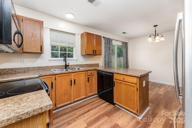 kitchen featuring a sink, black dishwasher, a peninsula, light wood finished floors, and stainless steel refrigerator