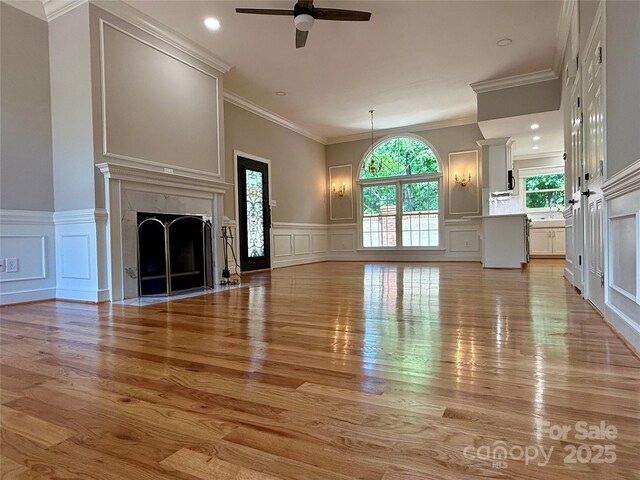 456 Brook Valley Ct NE, Concord, NC 28025 - unfurnished living room with a decorative wall, light wood-style floors, ceiling fan, a premium fireplace, and wainscoting