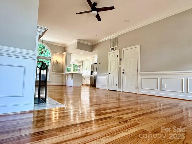 456 Brook Valley Ct NE, Concord, NC 28025 - unfurnished living room with a decorative wall, ornamental molding, light wood-style floors, a ceiling fan, and a wainscoted wall