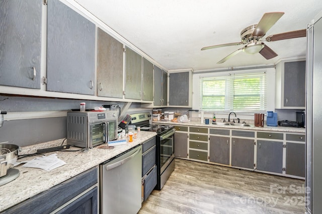 kitchen featuring appliances with stainless steel finishes, a sink, light wood-type flooring, a ceiling fan, and gray cabinetry