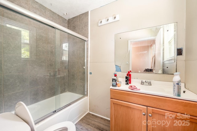 bathroom featuring toilet, enclosed tub / shower combo, vanity, wood finished floors, and baseboards