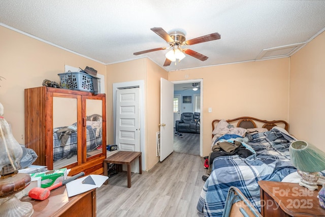 bedroom with light wood-style floors, ornamental molding, attic access, ceiling fan, and a textured ceiling