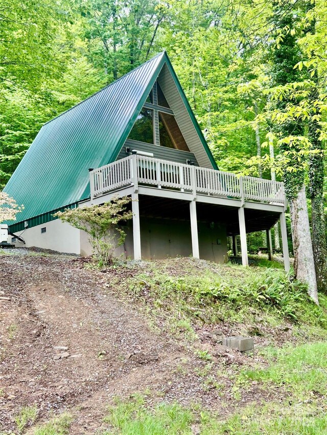 view of property exterior with a wooden deck, metal roof, a standing seam roof, and a view of trees