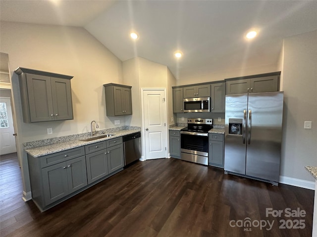 kitchen with stainless steel appliances, a sink, gray cabinets, vaulted ceiling, and dark wood-style flooring
