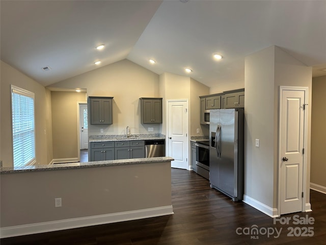 kitchen featuring stainless steel appliances, gray cabinetry, a sink, vaulted ceiling, and light stone countertops