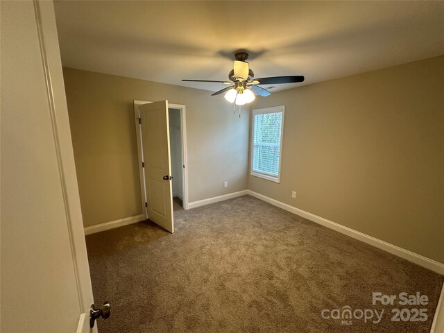 unfurnished room with ceiling fan, dark colored carpet, and baseboards