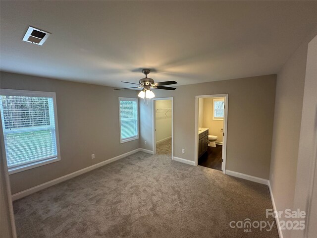 unfurnished bedroom with dark colored carpet, a walk in closet, baseboards, ensuite bath, and a closet