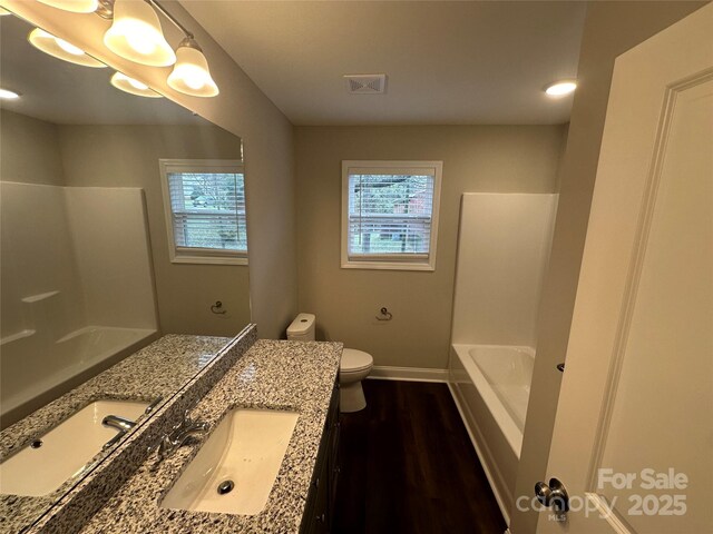 bathroom with healthy amount of natural light, vanity, wood finished floors, and toilet
