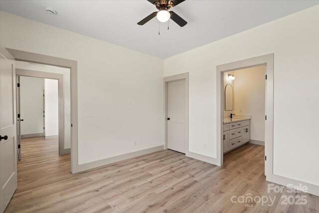 unfurnished bedroom featuring light wood-style floors, baseboards, ensuite bathroom, and ceiling fan