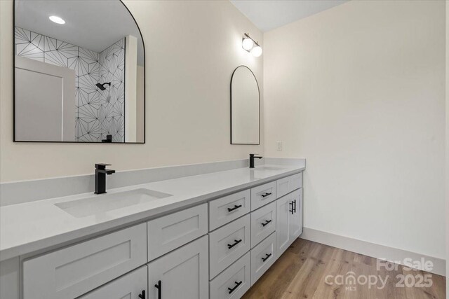 full bath with double vanity, wood finished floors, baseboards, and a tile shower