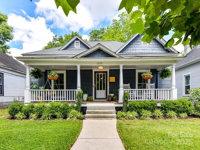 view of front of house with covered porch, a front lawn, and roof with shingles