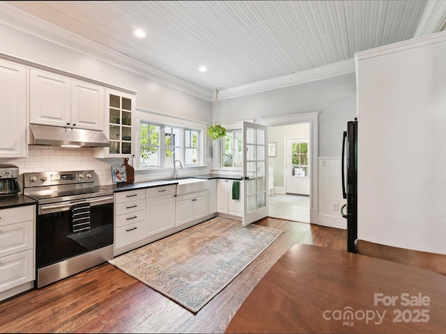 kitchen featuring stainless steel electric range oven, under cabinet range hood, dark countertops, a sink, and crown molding