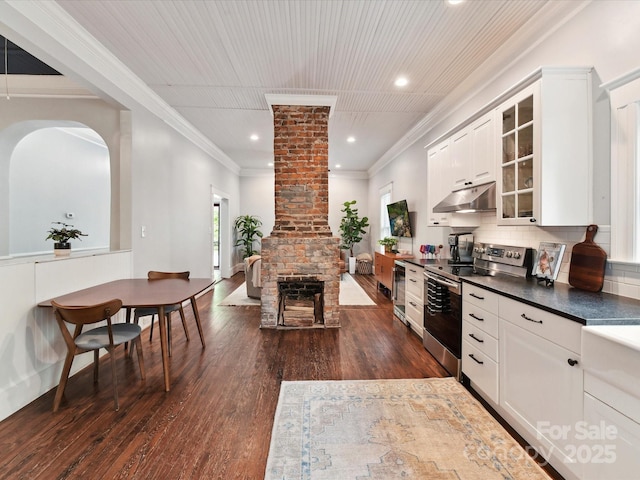 kitchen featuring stainless steel electric stove, under cabinet range hood, dark countertops, glass insert cabinets, and dark wood-type flooring