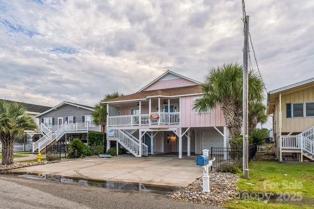 coastal inspired home with stairs, covered porch, an attached garage, and driveway
