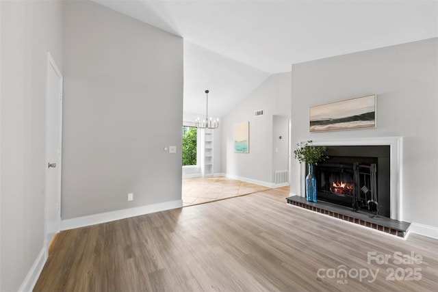 unfurnished living room featuring lofted ceiling, wood finished floors, a chandelier, baseboards, and a warm lit fireplace