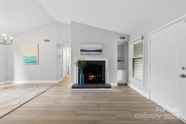 unfurnished living room with lofted ceiling, wood finished floors, a warm lit fireplace, baseboards, and built in features