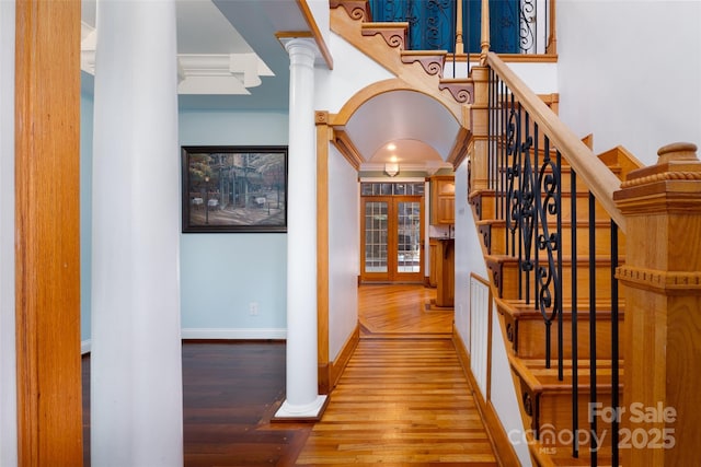 hallway with wood finished floors, crown molding, stairs, baseboards, and ornate columns