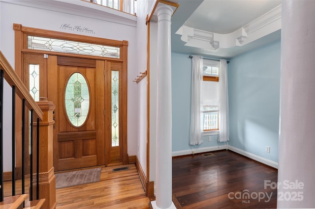 foyer featuring wood finished floors, ornate columns, baseboards, and stairs