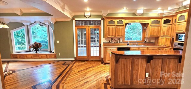 kitchen featuring ornamental molding, stainless steel appliances, light wood-style flooring, a sink, and glass insert cabinets