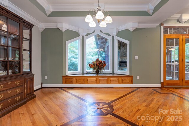 unfurnished dining area featuring light wood finished floors, ornamental molding, a chandelier, and baseboards