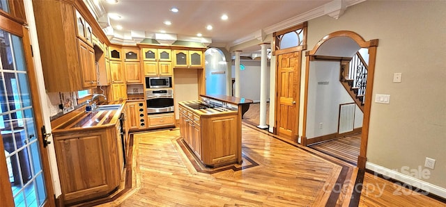 kitchen featuring appliances with stainless steel finishes, a sink, crown molding, light wood finished floors, and decorative columns