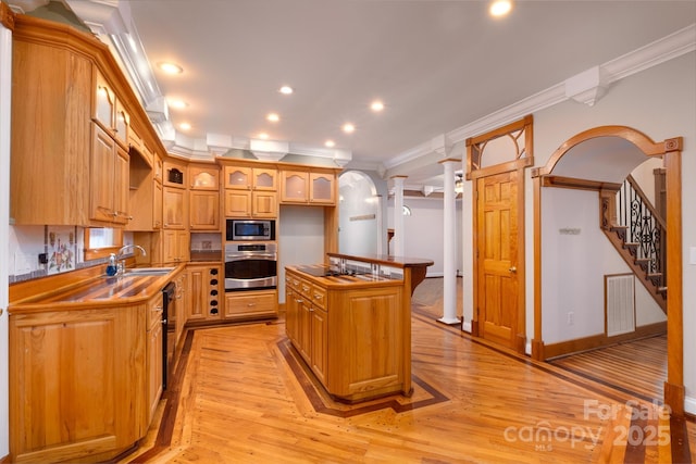 kitchen with appliances with stainless steel finishes, ornamental molding, a sink, light wood finished floors, and a center island