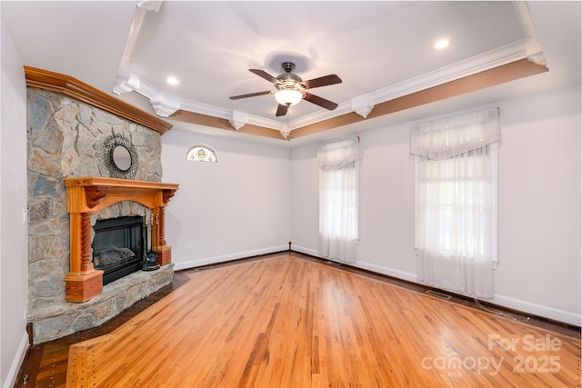 unfurnished living room featuring ornamental molding, wood-type flooring, a ceiling fan, a stone fireplace, and baseboards