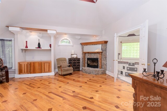 living area with light wood finished floors, a stone fireplace, and baseboards