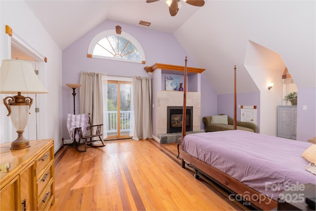 bedroom featuring vaulted ceiling, access to exterior, light wood-style floors, a tile fireplace, and ceiling fan
