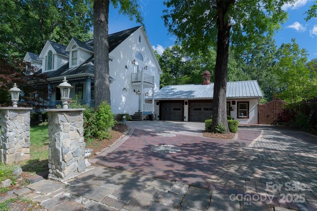 view of front facade with decorative driveway, a chimney, metal roof, fence, and an attached garage