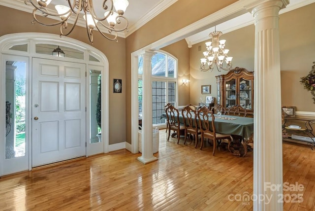 foyer entrance with a chandelier, ornate columns, crown molding, light wood finished floors, and a high ceiling