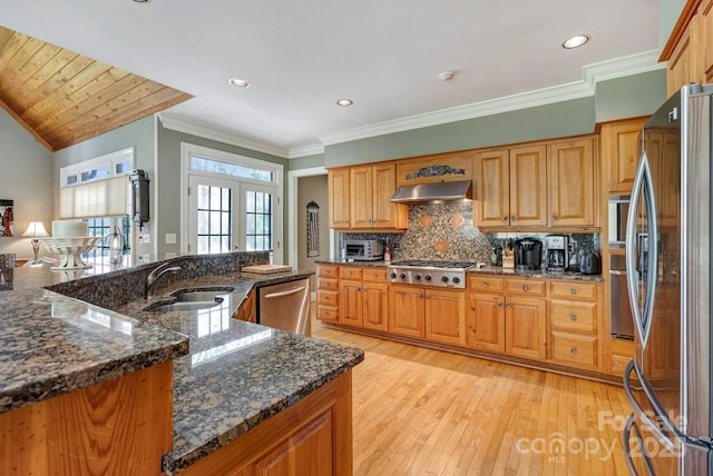 kitchen featuring appliances with stainless steel finishes, a sink, light wood-type flooring, tasteful backsplash, and under cabinet range hood