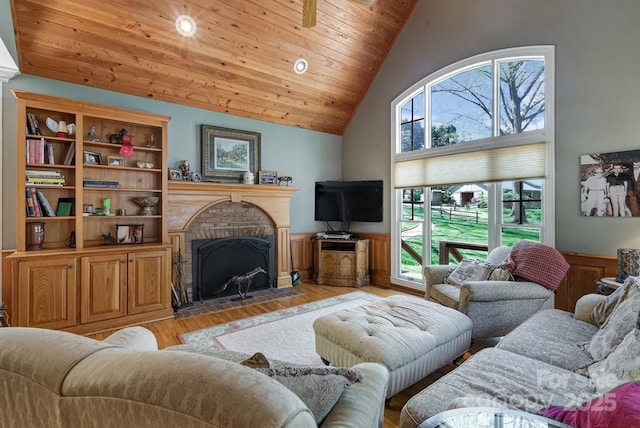 living area with a wainscoted wall, a brick fireplace, light wood-style floors, high vaulted ceiling, and wood ceiling